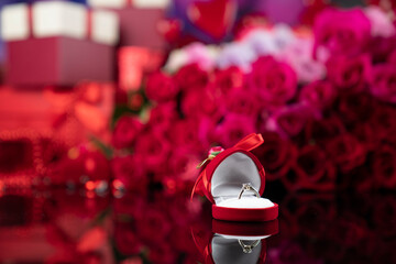 Romantic day concept. Engagement ring lying on shining table on the red roses background. 