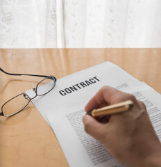 Hand holding a pen and a contract on the table