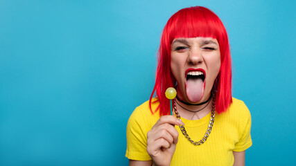 A bright and funny young woman with red hair licks a lollipop. Studio colorful picture of a pin-up style woman with a lollipop on a stick, on a blue background. A place for your text. - Powered by Adobe