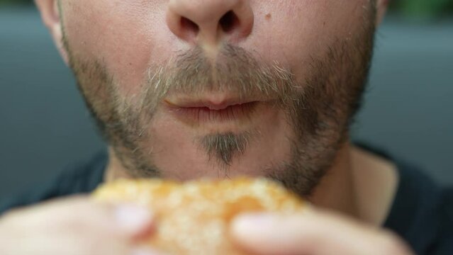 Man eating burger in restaurant. Close up shot of male biting hamburger. Hungry man