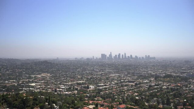 Zoomed in panning right view of the LA skyline from the Griffith Observatory with blue sky and lots of houses and neighborhoods.