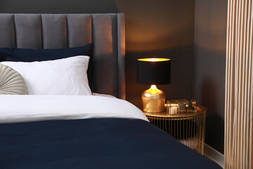 Comfortable bed with cushions, lamp and different decor on bedside table in room. Stylish interior