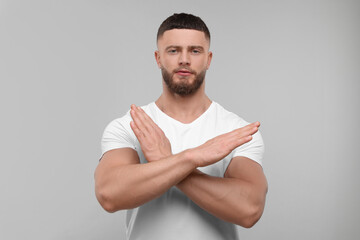 Stop gesture. Man with crossed hands on light grey background