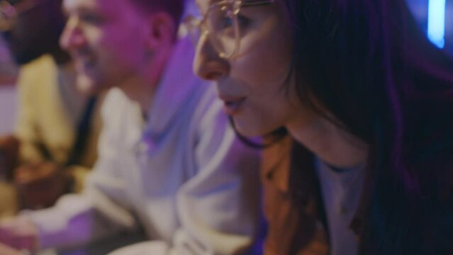 Close-up tilting shot of hands and face of excited young biracial girl sitting on couch and playing video game on console and wireless controller with Caucasian male friend, enjoying and smiling