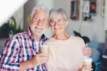 Happy senior white-haired couple embracing at home enjoying a coffee cup. Forever love, elderly couple in love