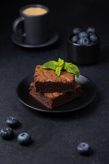 Chocolate brownie cake with mint, blueberries and espresso. Traditional American dessert. Popular cake with dark chocolate on a black background. Close-up, selective focus.