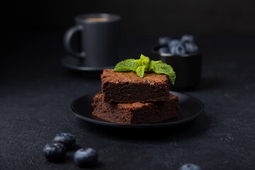 Chocolate brownie cake with mint, blueberries and espresso. Traditional American dessert. Popular cake with dark chocolate on a black background. Close-up, selective focus.