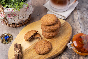 Oatmeal raisin cookies on a wooden board with cinnamon (cassia) sticks and a cup of milk. Traditional homemade pastry in rustic style. Selective focus, close-up.