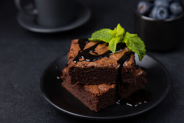 Chocolate brownie cake with mint, blueberries, chocolate topping and espresso. Traditional American dessert. Popular cake with dark chocolate on a black background. Close-up, selective focus.