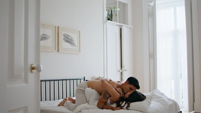 Loving guy kissing wife at bed. Romantic lovers flirting at pillows bedroom