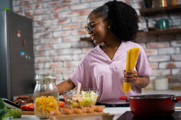 Young woman in kitchen. Beautiful African woman cooking pasta..