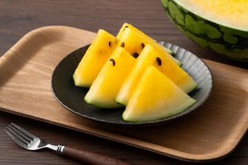 Sliced yellow watermelon in a plate on wooden table background.