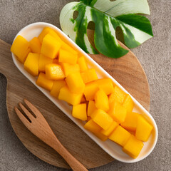 Fresh chopped, diced mango cubes on gray table background with tropical leaf.
