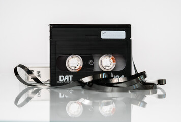 Front view of a DAT (digital audio cassette) cassette with a box and a twisted tape stands upright...