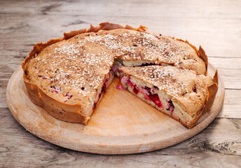 Rustic homemade cherry and cherry plum pie sprinkled with sesame seeds on a round cutting board on an old wooden table. Country style.