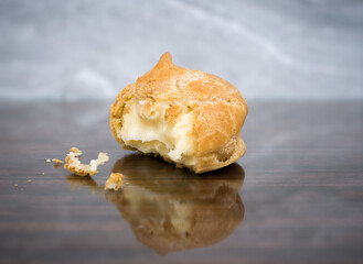Bitten freshly baked custard profiterole on a polished tabletop with reflection