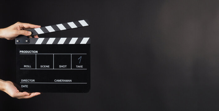 Hand is holding Black clap board or movie slate  use in video production , movie ,film, cinema industry on black background.It have write in number.