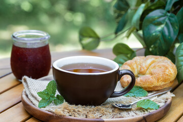 Cup of tea with mint, croissant and jar of jam