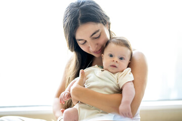 Young mother holding her newborn baby boy at home in living room.