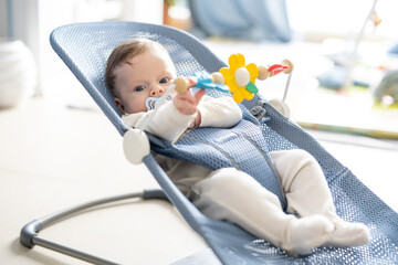 Adorable 5 months old baby boy sitting in his swing rocking chair, playing with rotating toys.