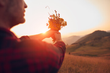 Man holding field flowers in nature.