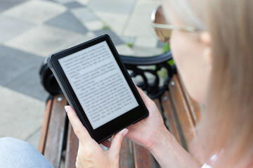  woman reading an e-book sitting on a park bench.