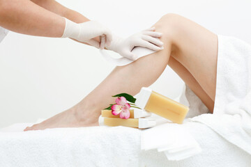 Woman or girl having hair removal procedure on leg with wax depilatory in white salon. Depilation concept. Close up cosmetologist's hands