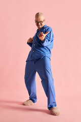 Fototapeta premium Full body shoot of funny man in pajama playing imaginary guitar over pastel rose background.