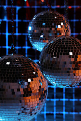 Shiny disco balls against foil party curtain under color lights