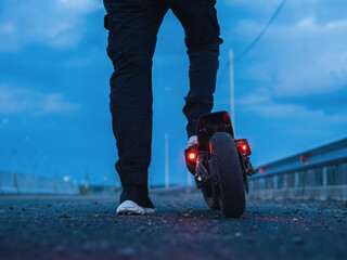 A man stands on an electric scooter, rear view. Overcast sky. Drive on the road