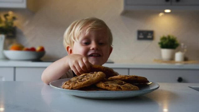 Mischievous young boy taking giant cookie from plate in kitchen at home - shot in slow motion