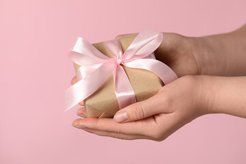 Woman holding gift box with bow on pink background, closeup