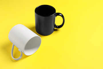 Black and white ceramic mugs on yellow background. Space for text