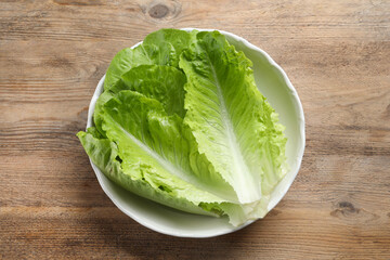 Bowl with fresh leaves of green romaine lettuce on wooden table, top view