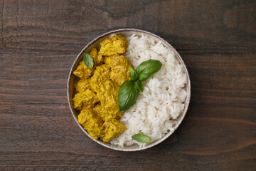 Delicious rice and chicken with curry sauce on wooden table, top view