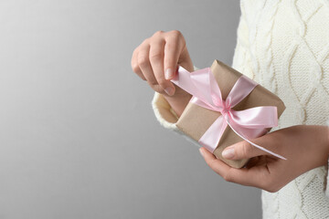 Woman holding gift box with pink bow on light grey background, closeup. Space for text