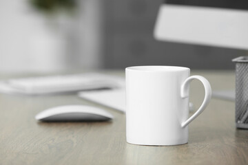 White ceramic mug on wooden table at workplace. Mockup for design