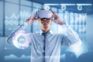 Attractive smiling young european businessman with VR glasses and glowing business chart hologram on blurry office interior backdrop. Virtual reality, finance and metaverse concept. Double exposure.