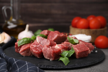 Cut fresh beef meat with basil and spices on brown table, closeup