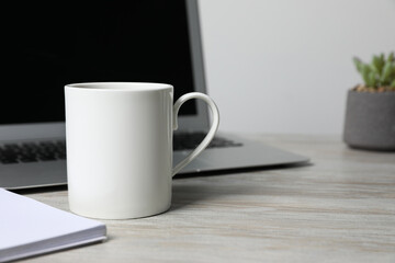 Ceramic mug, laptop and notebook on white wooden table, closeup. Space for text