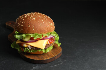 Delicious burger with beef patty and lettuce on dark table, space for text