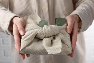 Furoshiki technique. Woman holding gift packed in fabric and decorated with eucalyptus branch,...
