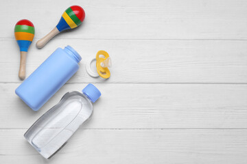 Baby powder, oil, pacifier and toys on white wooden table, flat lay. Space for text