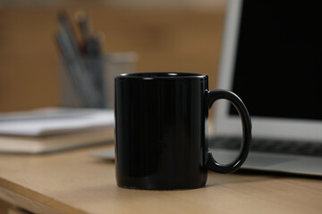 Black ceramic mug and laptop on wooden table at workplace