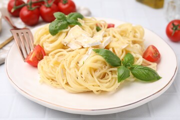 Delicious pasta with brie cheese, tomatoes and basil leaves on white tiled table, closeup