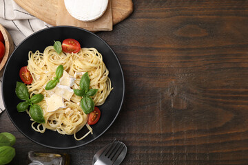 Delicious pasta with brie cheese, tomatoes and basil leaves served on wooden table, flat lay. Space...