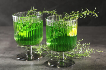 Glasses of homemade refreshing tarragon drink and sprigs on grey table, closeup