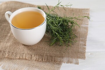 Aromatic herbal tea and fresh tarragon sprigs on white wooden table