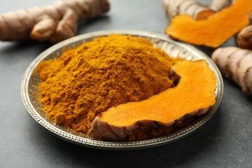 Plate with turmeric powder and cut root on grey table, closeup