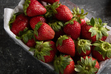 photo of many juicy, fresh, ripe strawberries in a plastic container, top view, vertical photo